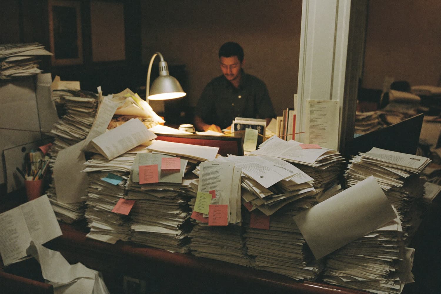 A front desk before dawn, buried in printed lists and papers under too many screens.